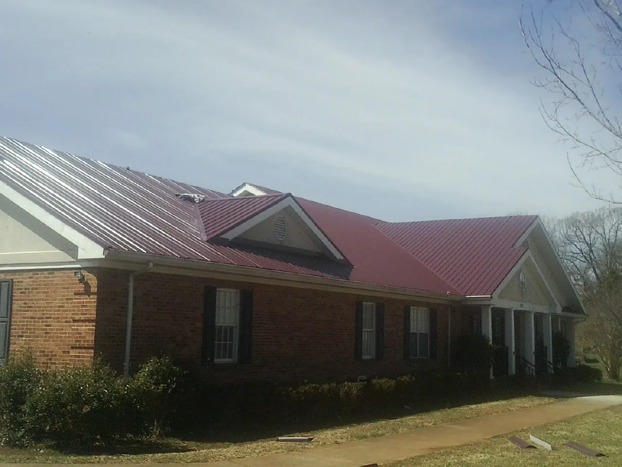 Red metal roof with gabled entries on a long brick building, from a Hail Damage Roof Repair job in Pratts