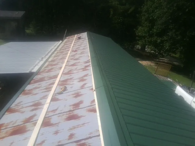 Old rusted panels beside newly installed green metal roofing — Wind Damage Roof Repair by Roofing Brothers in Pratts