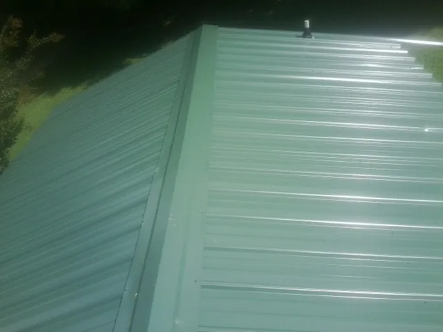 New green metal panels meeting at the ridge of a roof — Flat Roof Repair work by our crew in Pratts