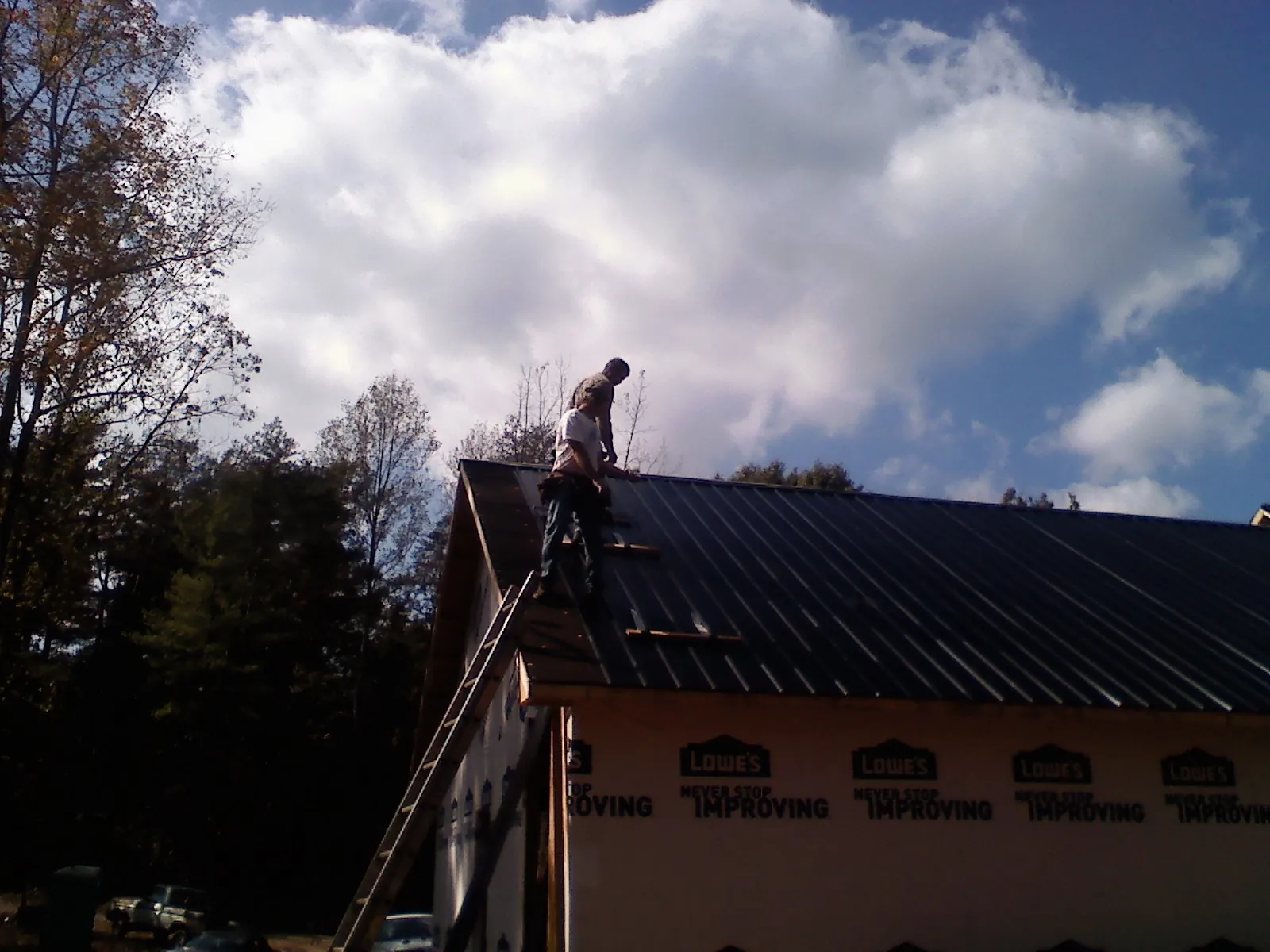 Roofer fastening dark metal panels high against a cloudy sky, from a Roof Inspection job in Pratts